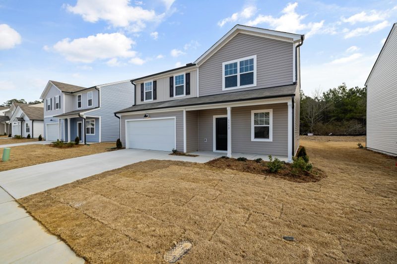 A modern suburban home with a garage, under a clear blue sky, features a dry grass lawn